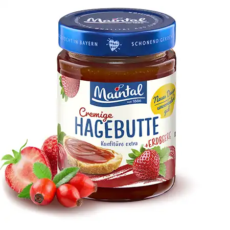 Glas of Maintal 340g Rosehip-strawberry preserve extra and next to it fresh rosehips and strawberries.